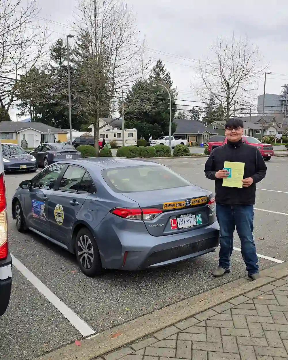 Student holding road test paperwork beside the Right of Way driving school car