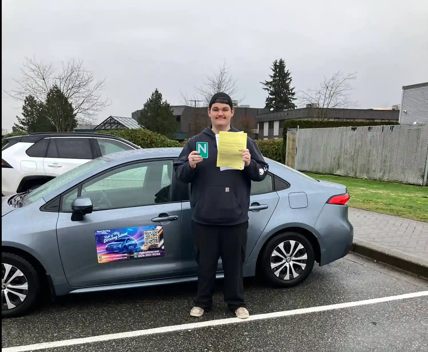 Happy student holding his N sign beside the driving school car